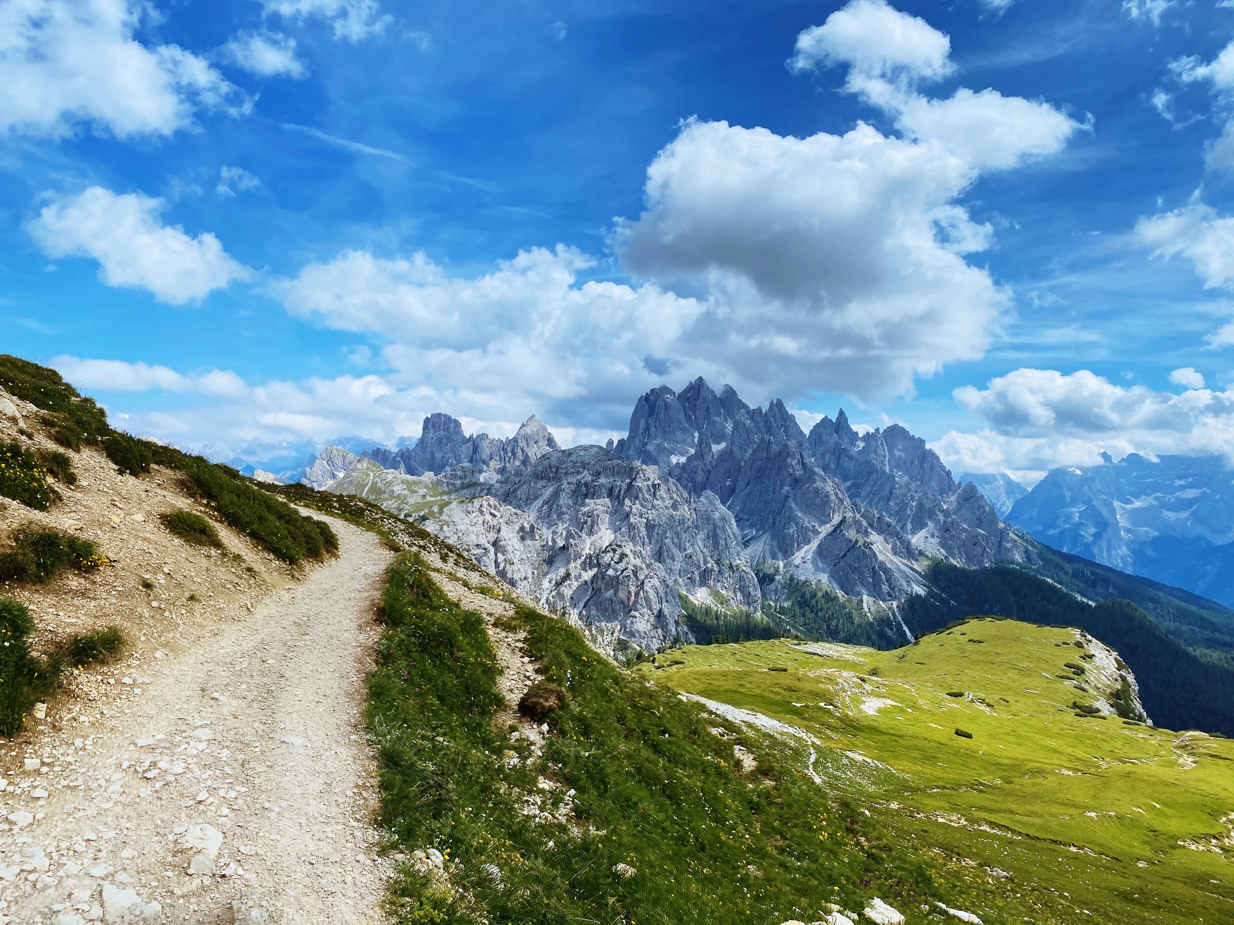 An Alpine trail overlooking dramatic rocky peaks and green meadows