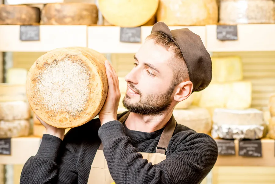 Cheesemaker holding a large wheel of cheese in his shop