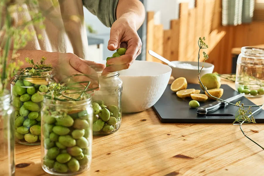 Hands preparing jars of green olives with herbs