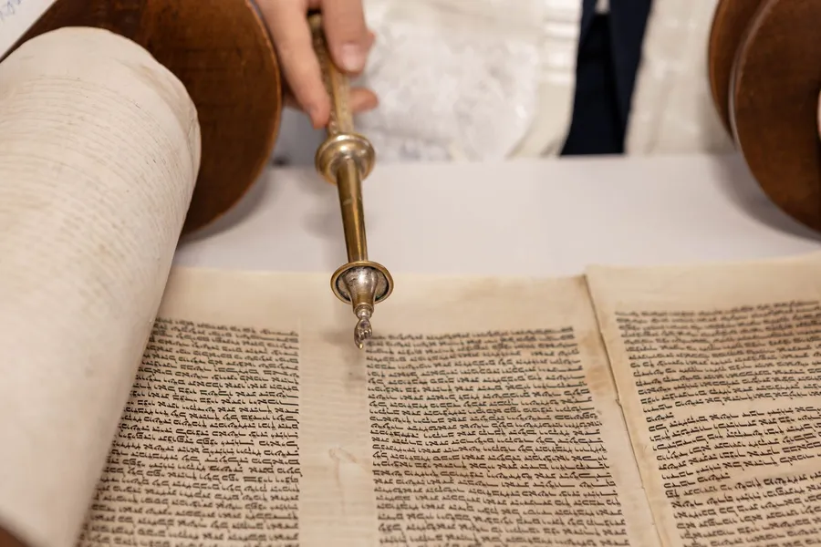 A hand following handwritten text on parchment with a pointer